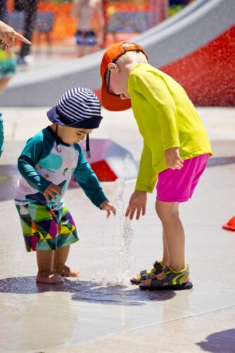 two little kids playing in water spraying up from the ground